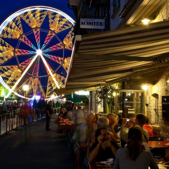 Thun bei Nacht am Aarequai mit Blick Richtung Mühleplatz und auf buntes, grosses Riesenrad.