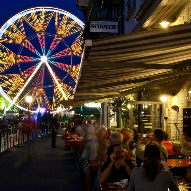 Thun bei Nacht am Aarequai mit Blick Richtung Mühleplatz und auf buntes, grosses Riesenrad.