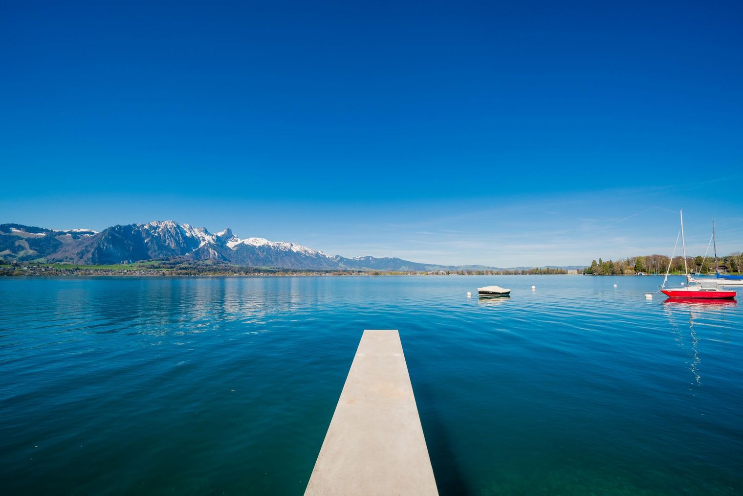 Steg ragt in den tiefblauen Thunersee hinaus und bietet Ausblick auf Stockhorn und vorbeiziehende Schiffe