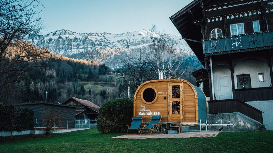Saunakiste vor einem Haus und der verschneiten Bergkette in Leissigen