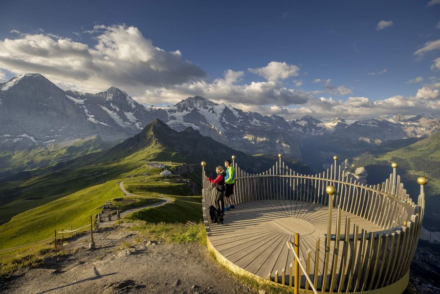 Ein wanderndes Paar bewundert von der kronenförmigen Aussichtsplattform die Bergwelt mit Eiger, Mönch und Jungfrau im Hintergrund. 