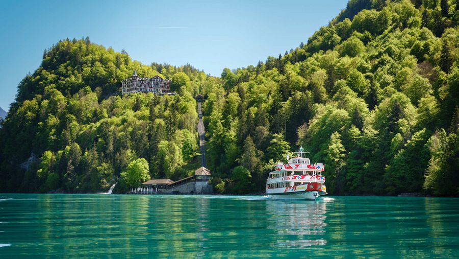 Ein Schiff auf dem türkisen Brienzersee und im grünen Wald das Grandhotel Giessbach