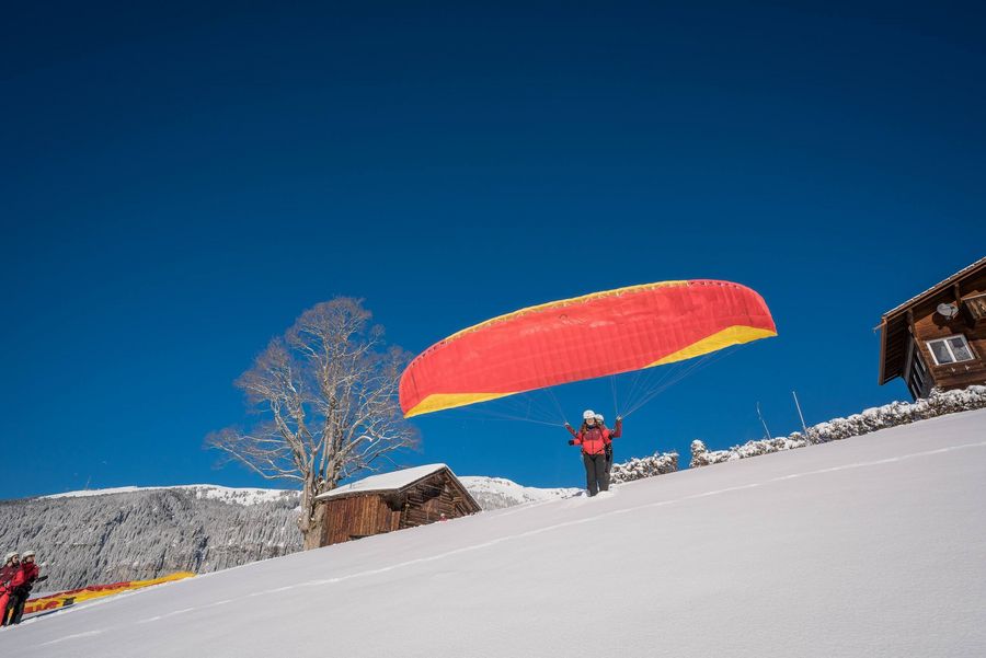 [Translate to Englisch:] Paraglidingpilot startet den Flug im verschneiten Amisbühl bei Beatenberg