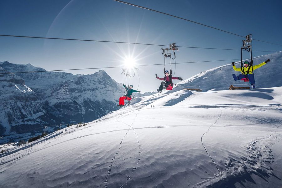 Drei Gäste fliegen mit dem First Flyer durch die verschneite Winterlandschaft mit Bergpanorama