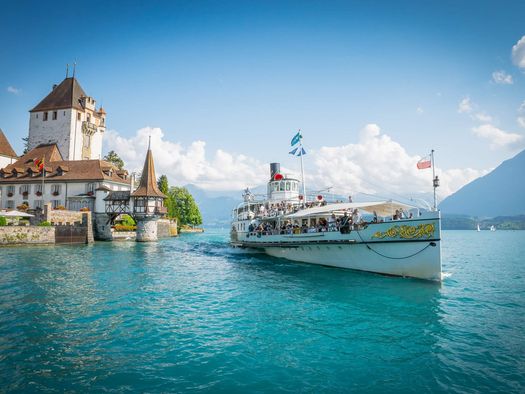 Märchenhaftes Schloss Oberhofen mit Dampfschiff Blümlisalp, das über den Thunersee gleitet. Im Hintergrund der Niesen.